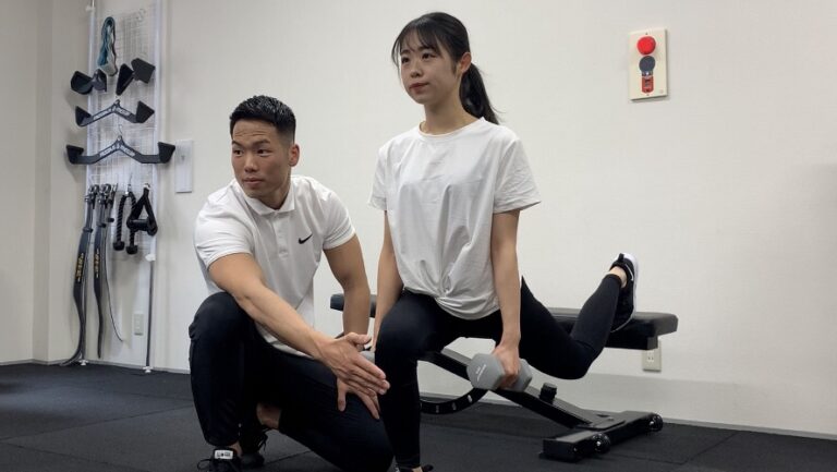 トレーナーがマンツーマンでスクワットのフォームを指導する様子